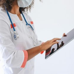 A doctor wearing a face mask and stethoscope using a tablet in a medical setting.