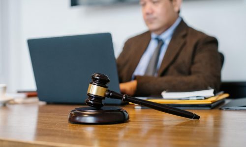 Crop concentrated Asian male judge in formal clothes sitting using modern netbook while working in law office