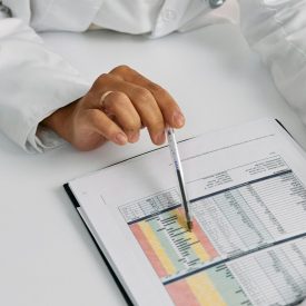 Doctor analyzing patient charts with a pen, focusing on data points for medical insights.