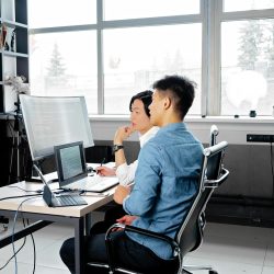 Two men analyzing code on computers in a modern office setting.