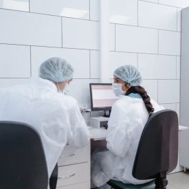 Two scientists in PPE discussing research at a computer in a laboratory setting.